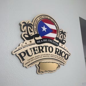 May include: Wooden sign featuring the Puerto Rican flag and the words "Puerto Rico" and "Isla Del Encanto." The sign includes a gold-colored map of Puerto Rico and lists traditional dishes. The sign is mounted on a wall.