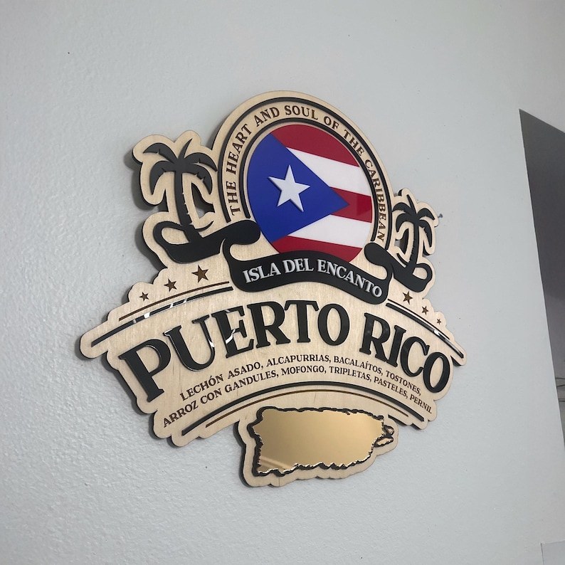 May include: Wooden sign featuring the Puerto Rican flag and the words "Puerto Rico" and "Isla Del Encanto." The sign includes a gold-colored map of Puerto Rico and lists traditional dishes. The sign is mounted on a wall.