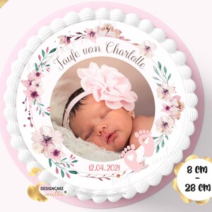May include: A white cake with a pink and green floral design and a photo of a baby girl in the center. The cake is decorated with the text "Taufe von Charlotte" and the date "12.04.2021". The cake is 8 inches in diameter and 28 inches in circumference.