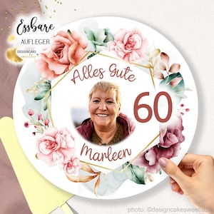 Könnte beinhalten: Ein runder essbarer Tortendekor mit einem floralen Design in Rosa-, Grün- und Goldtönen. Der Dekor zeigt ein Foto einer Frau mit dem Text "Alles Gute 60 Marleen" in der Mitte.