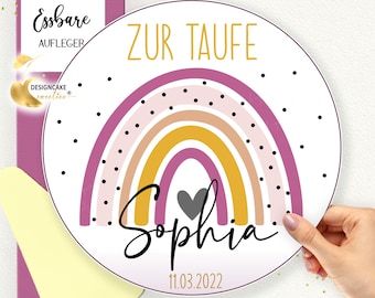 May include: Round edible cake topper with a rainbow design in pink, orange, yellow, and purple with black polka dots. The text "Zur Taufe" is at the top of the topper, and the name "Sophia" is written in cursive with a grey heart below the rainbow. The date "11.03.2022" is at the bottom of the topper.