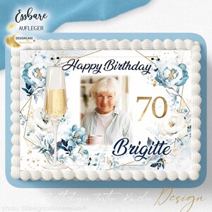 Könnte beinhalten: Ein rechteckiger Kuchen mit hellblauem Rand und weißer Zuckergussverzierung. Der Kuchen zeigt ein Foto einer Frau, die Worte "Happy Birthday", die Zahl "70" und den Namen "Brigitte" sowie florale und geometrische Designs.