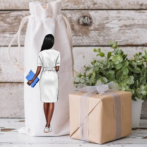 Puede incluir: Una bolsa blanca con cord&oacute;n con una ilustraci&oacute;n de una persona con un vestido blanco sosteniendo una carpeta azul. En la imagen tambi&eacute;n hay una caja de regalo envuelta con una cinta plateada y una peque&ntilde;a planta en maceta.
