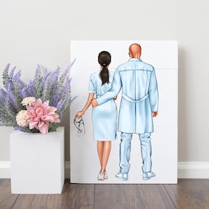Puede incluir: Ilustraci&oacute;n de una pareja de profesionales de la salud, un m&eacute;dico y una enfermera, con uniforme m&eacute;dico azul claro. La enfermera sostiene un estetoscopio. La obra de arte est&aacute; sobre un panel de madera blanco. Un jarr&oacute;n cuadrado blanco contiene flores de lavanda y rosas.