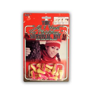 Puede incluir: Un paquete blíster rojo etiquetado como The All I Want For Christmas Survival Kit con una fotografía de una persona con gorro y bufanda rojos. El envase contiene una colección de tapones para los oídos de espuma pequeños, amarillos y rosas.
