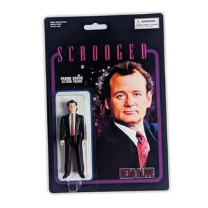 May include: A vintage action figure of Frank Cross from the movie "Scrooged" in its original packaging. The packaging is black with the movie title and a picture of Bill Murray. The figure is wearing a black suit and red tie.