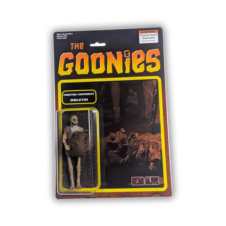May include: A vintage-style action figure of the Chester Copperpot Skeleton from "The Goonies." The figure is in a clear plastic case attached to a retro-themed card. The card features the movie's logo and a warning about small parts.
