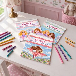 May include: Three spiral-bound coloring books titled Emmy's Magical Friends Coloring Book, Emmy's Mermaid Coloring Book, and Emmy's Superhero Coloring Book, arranged with assorted colored pencils and crayons on a white surface.
