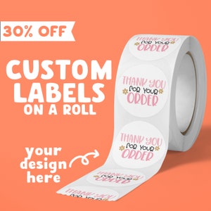Op de afbeelding: Een rol witte ronde stickers met de tekst "Bedankt voor uw bestelling" in roze letters met kleine roze bloemen. De stickers zitten op een witte rol met een roze achtergrond.