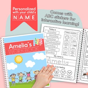 May include: A personalized workbook with the name "Amelia" on the cover, featuring a sunny sky and children playing. The workbook includes ABC stickers for interactive learning and pages for writing practice.
