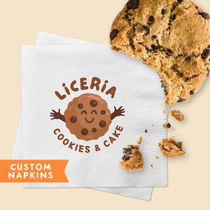 Könnte beinhalten: Weiße Papierserviette mit einem braunen Comic-Cookie mit einem lächelnden Gesicht und dem aufgedruckten Text "Liceria Cookies & Cake". Die Serviette ist in der Mitte gefaltet und unten links steht der Text "Custom Napkins". Auf der Serviette liegt ein Schokoladenchip-Cookie.