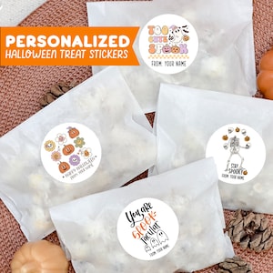Op de afbeelding: Vier witte papieren zakken met ronde Halloween-stickers. De stickers bevatten illustraties van pompoenen, geesten, skeletten en de tekst "Too Cute to Spook", "Happy Halloween", "You are Spooktacular" en "Stay Spooky".