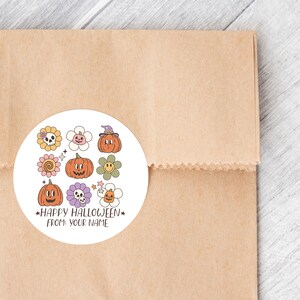 Op de afbeelding: Een ronde witte sticker met een Halloween-thema. Het bevat verschillende illustraties, waaronder pompoenen, bloemen en schedels. De tekst op de sticker luidt "Happy Halloween" en "From: Your Name".