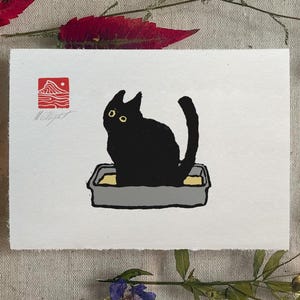 Puede incluir: Ilustración de un gato negro sentado en una caja de arena sobre un fondo blanco. El gato tiene ojos amarillos y está en una caja de arena gris con arena amarilla. La obra de arte tiene un sello rojo y el texto "MATEUSZOLBRYCHT".
