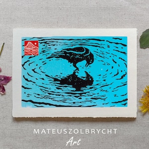 May include: A black and blue art print featuring a bird reflected in water. The print has a red square with a mountain design in the upper left corner. The artist's name and the word "Art" are at the bottom.