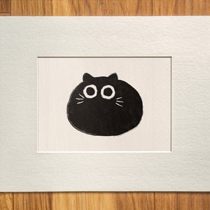 May include: A black and white illustration of a round, cartoon cat with large eyes and whiskers.