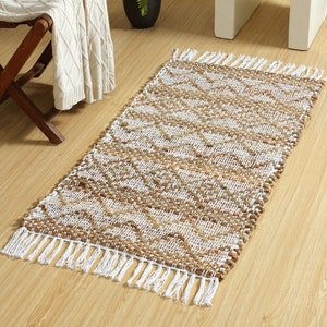 May include: A natural fiber rug with a white and brown woven pattern. The rug has white fringe on all sides.