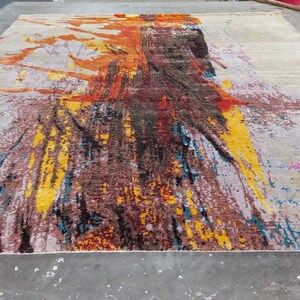 May include: Abstract area rug with a colorful design featuring shades of yellow, orange, red, blue, and pink. The rug has a white background with a distressed look.