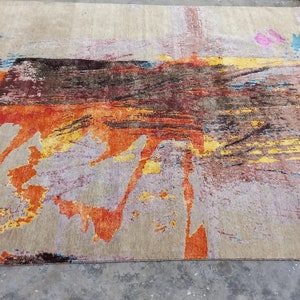 May include: Abstract area rug with a beige background and colorful abstract designs in shades of orange, yellow, blue, and brown.