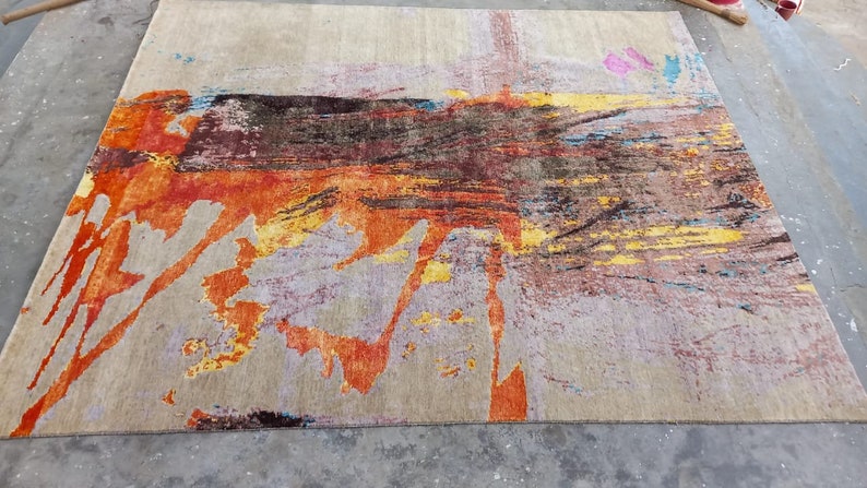 May include: Abstract area rug with a beige background and colorful abstract designs in shades of orange, yellow, blue, and brown.