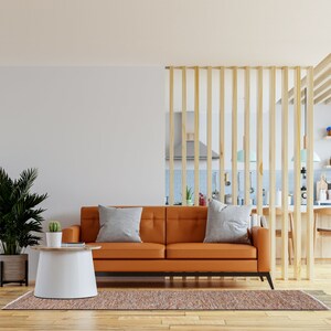 K&ouml;nnte beinhalten: Ein modernes Wohnzimmer mit einem orangefarbenen Ledersofa und zwei grauen Kissen. Ein wei&szlig;er und h&ouml;lzerner Beistelltisch beherbergt einen kleinen Kaktus. Ein gemusterter Teppich und eine gro&szlig;e Topfpflanze vervollst&auml;ndigen die Einrichtung. Ein Holzlatten-Teiler trennt das Wohnzimmer von der K&uuml;che.