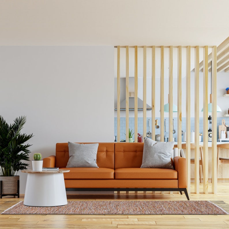 K&ouml;nnte beinhalten: Ein modernes Wohnzimmer mit einem orangefarbenen Ledersofa und zwei grauen Kissen. Ein wei&szlig;er und h&ouml;lzerner Beistelltisch beherbergt einen kleinen Kaktus. Ein gemusterter Teppich und eine gro&szlig;e Topfpflanze vervollst&auml;ndigen die Einrichtung. Ein Holzlatten-Teiler trennt das Wohnzimmer von der K&uuml;che.