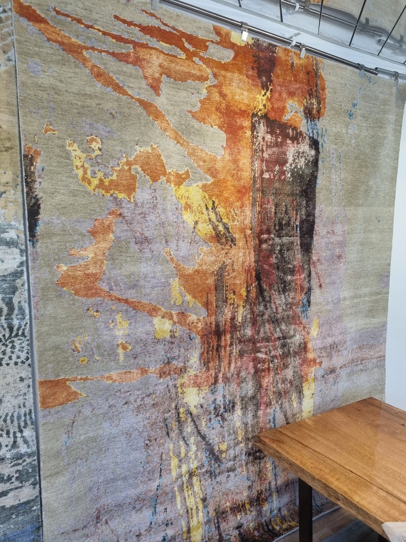 May include: Abstract rug with a gray background and orange, yellow, and blue abstract designs. The rug is hanging on a wall.
