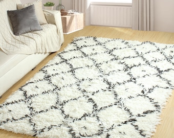 Op de afbeelding: Wit shag tapijt met een zwart geometrisch patroon. Het tapijt heeft een zachte, pluche textuur en is perfect om elke kamer een vleugje moderne stijl te geven.