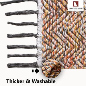 K&ouml;nnte beinhalten: Nahaufnahme eines gewebten Teppichs mit einem geometrischen Muster in Orange-, Wei&szlig;- und Braunt&ouml;nen. Der Teppich hat einen Fransenrand aus grauen Quasten an einer Kante. Der Text "Thicker & Washable" steht unten.