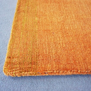 Op de afbeelding: Close-up van de rand van een verbrand oranje kleed met een iets lichtere oranje rand. Het kleed heeft een textuur, geweven uiterlijk.
