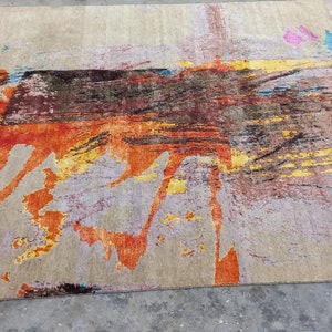 May include: Abstract area rug with a beige background and colorful abstract designs in shades of orange, yellow, blue, and brown.