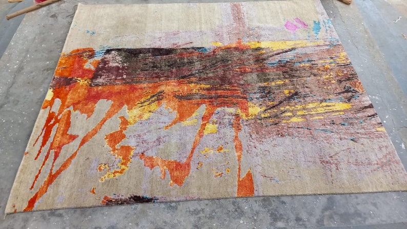 May include: Abstract area rug with a beige background and colorful abstract designs in shades of orange, yellow, blue, and brown.