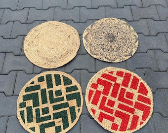 Op de afbeelding: Vier ronde jute placemats. Eén is effen, twee hebben geometrische ontwerpen in groen en rood, en één heeft een zwart mandala patroon. De placemats zijn gemaakt van natuurlijke vezels en zijn geschikt voor woondecoratie.