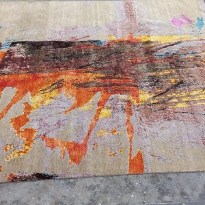 May include: Abstract area rug with a beige background and splashes of orange, yellow, blue, and pink.