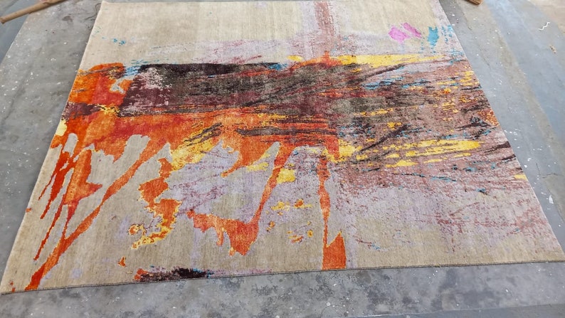 May include: Abstract area rug with a beige background and splashes of orange, yellow, blue, and pink.