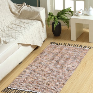 May include: A long, rectangular rug with a multicolored, textured pattern and fringe on both ends. The rug is laid out on a wooden floor in a living room setting.