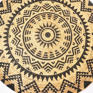 Könnte beinhalten: Ein runder, gewebter Teppich mit einem geometrischen Muster in Schwarz und Braun. Die Mitte des Teppichs zeigt ein Sonnenstrahlen-Design.