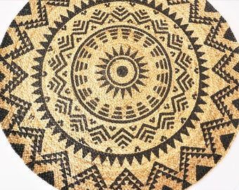 May include: A round, woven rug with a black and tan geometric pattern. The center of the rug features a sunburst design.