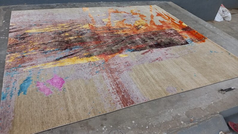 May include: Abstract area rug with a beige background and colorful abstract designs in shades of yellow, orange, pink, blue, and brown.