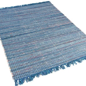 Puede incluir: Una alfombra tejida azul y blanca con borde de flecos. La alfombra tiene un sutil patrón de rayas finas y una superficie texturizada.