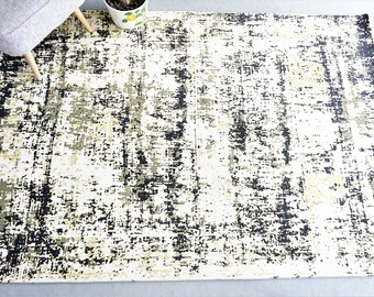 Op de afbeelding: Abstract vloerkleed met een witte achtergrond en een zwart en groen splatterontwerp.
