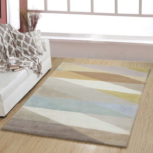 Op de afbeelding: Een geometrisch tapijt met beige, bruine en blauwe patronen met een diagonaal streepontwerp. Het tapijt ligt op een houten vloer.
