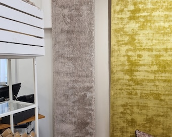 Puede incluir: Dos alfombras rectangulares largas colgadas en una pared. La alfombra de la izquierda es de color marrón claro con un brillo sutil. La alfombra de la derecha es de color amarillo brillante con un aspecto texturizado y desgastado.