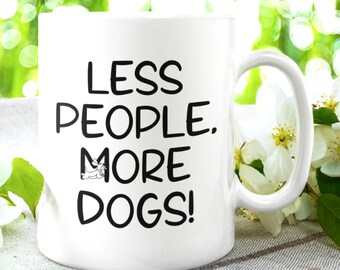 May include: White ceramic coffee mug with black text that reads "Less People. More Dogs!"  A small black and white dog illustration is next to the word "More".