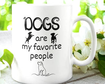 May include: White ceramic coffee mug with black text that reads "Dogs are my favorite people". The mug has a black silhouette of a dog in three different poses.