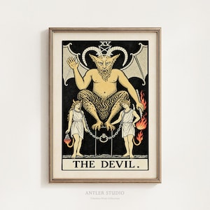 May include: A framed print of The Devil tarot card, featuring a central horned figure with wings perched on a pedestal above two chained figures. The artwork uses a black, cream, and orange color palette with the Roman numeral XV and text THE DEVIL.