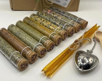 May include: A set of eight glass test tubes filled with various dried herbs and teas, each sealed with a cork stopper. Included are two honey sticks, a heart-shaped metal tea infuser, and a small wooden spoon with engraved text.