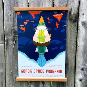 May include: A blue and green poster with a cartoon character in a rocket ship. The poster says "Korok Space Program" and lists locations from the video game "The Legend of Zelda: Breath of the Wild".