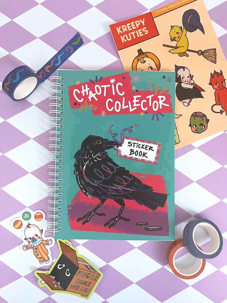 May include: A teal blue spiral bound notebook with the words "CHAOTIC COLLECTOR" and "STICKER BOOK" on the cover. The cover features a black crow with a red background. The notebook is surrounded by colorful washi tape and stickers.
