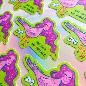 May include: A selection of stickers with a quirky design. Each sticker shows a woman with pink hair and a bird's body, set against a green background. The text "SHE SAID NO PICKLES" and "BEEFTOPIA" are included.